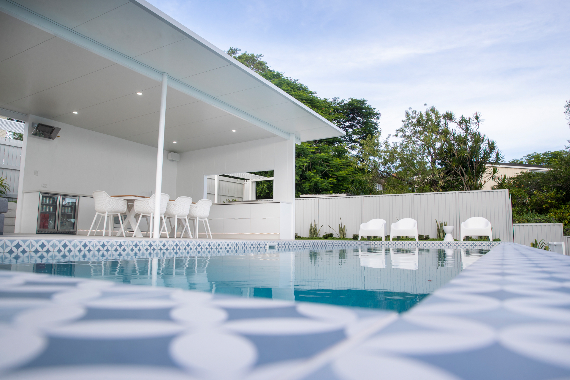 Renovated pool with patterned waterline tiling, white outdoor lounge chairs and a covered alfresco area, North Brisbane